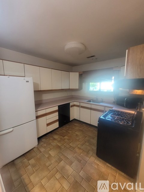 A kitchen with a white fridge and brown tiled floor.