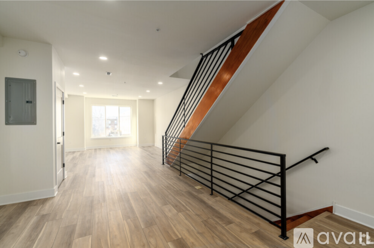 A spacious hallway with wooden floors and a staircase with black metal railings.