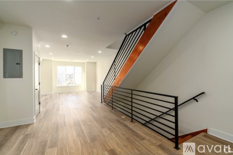 A spacious hallway with wooden floors and a staircase with black metal railings.