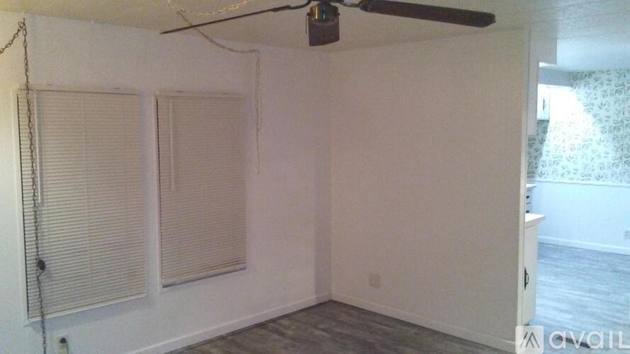 A room with a ceiling fan and two windows with blinds.