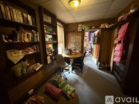 A room with a table, chairs, and a bookshelf filled with books and various items.