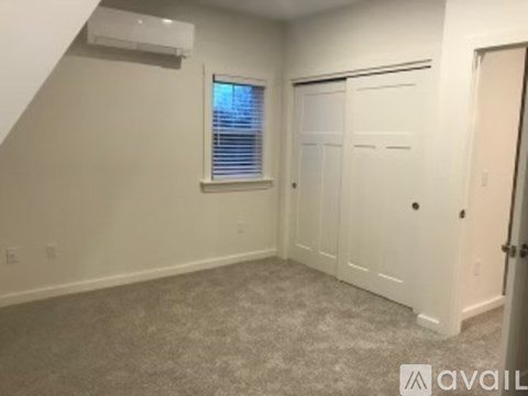 A room with a carpeted floor, a window with blinds, and a door.