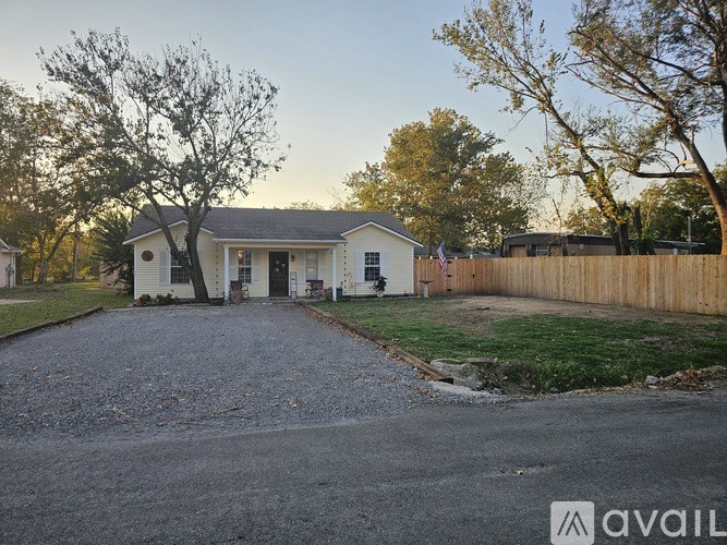 A house with a flag on the front porch is surrounded by a fence and trees.