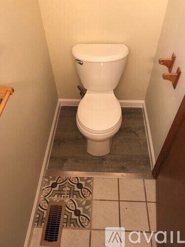 A white toilet in a small bathroom with a tiled floor and a wooden door.
