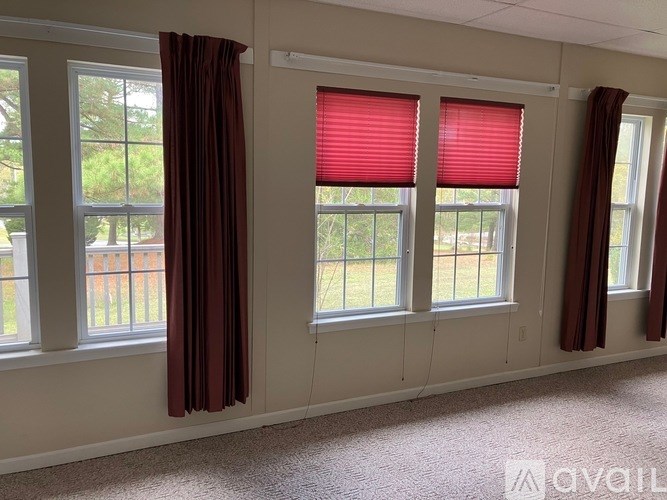A room with three windows, each with red blinds and brown curtains.