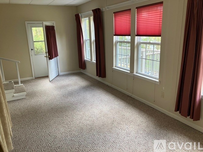 A room with a carpeted floor, two windows with red blinds, and a white door.