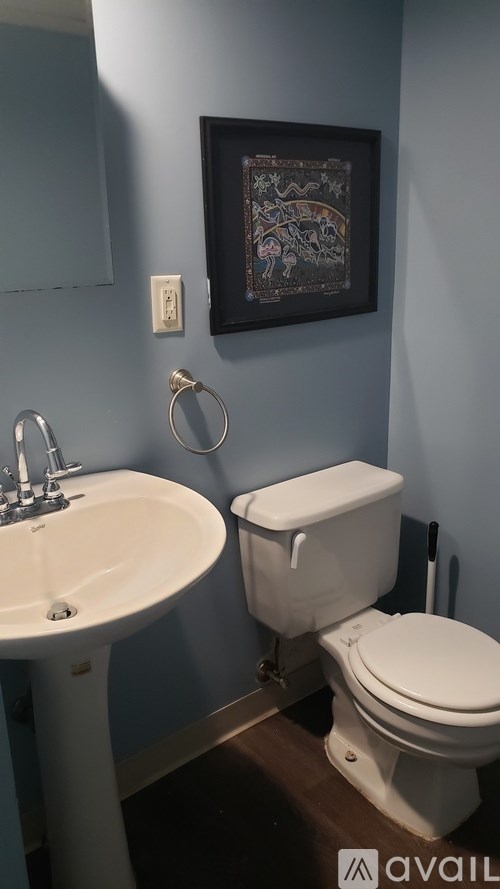 A bathroom with a toilet, sink, and a picture on the wall.