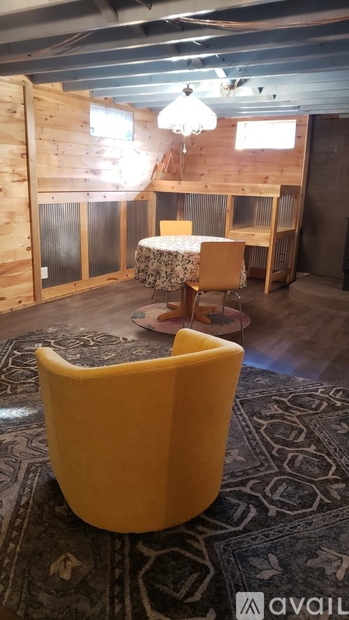 A yellow chair is in the foreground of a room with wooden walls.