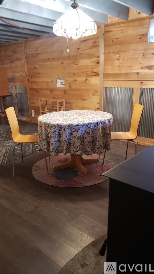 A round table with a floral tablecloth is surrounded by two chairs in a room with wooden walls.