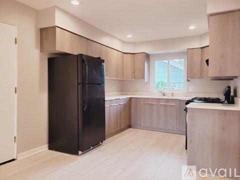 A black refrigerator is in a kitchen with wooden cabinets and a window.