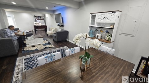 A woman is sitting on a couch in a living room with a television and a bed in the background.