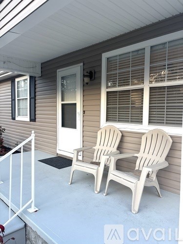 Two white chairs are on a porch.