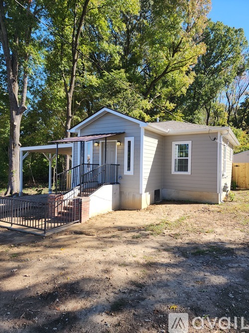 A house with a porch and a fence is surrounded by trees.