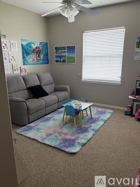 A living room with a grey couch, a small table with a painting on it, and a ceiling fan.