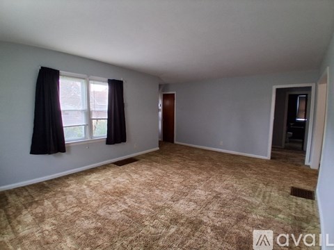 A room with a carpeted floor and a window with black curtains.