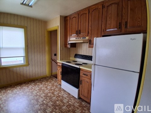 A kitchen with a white fridge, wooden cabinets, and a tiled floor.