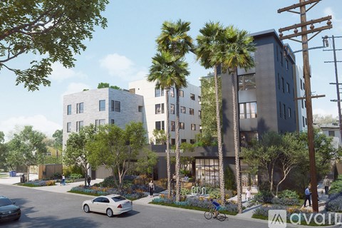 A street view of a residential area with apartment buildings, palm trees, and a person riding a bicycle.