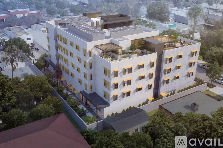 A modern multi-story building with balconies and a flat roof is surrounded by greenery.