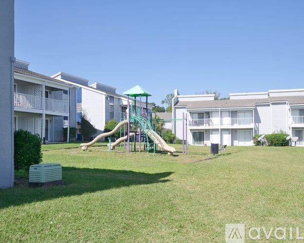 A playground with a green slide is in front of apartment buildings.