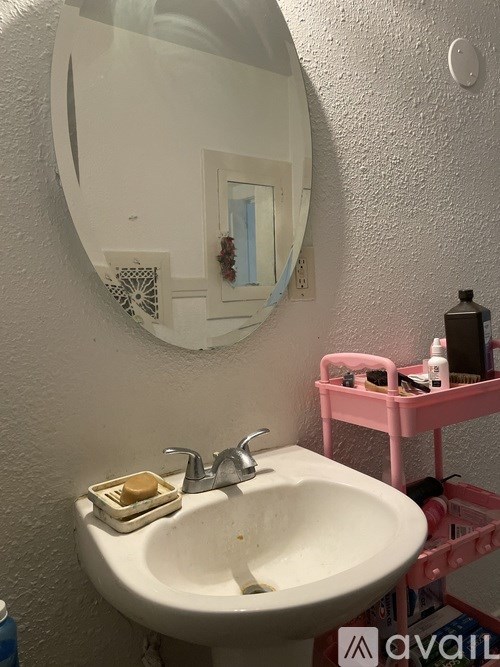A bathroom with a pink stool and a round mirror.