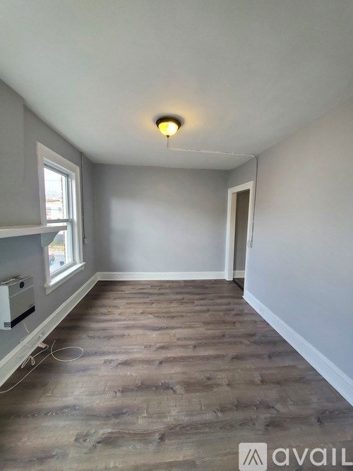 A room with wooden flooring and a window on the left side.