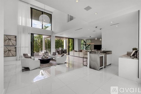 A modern living room with white furniture and a kitchen area in the background.