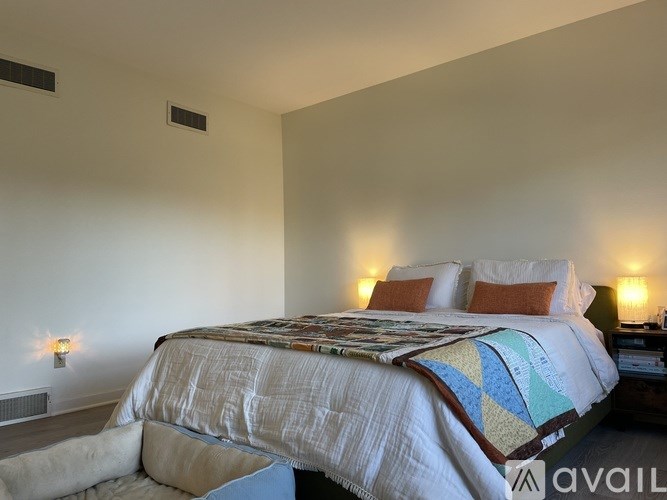 A bed with a white comforter and a blue and yellow quilt is in a room with two wall lamps.