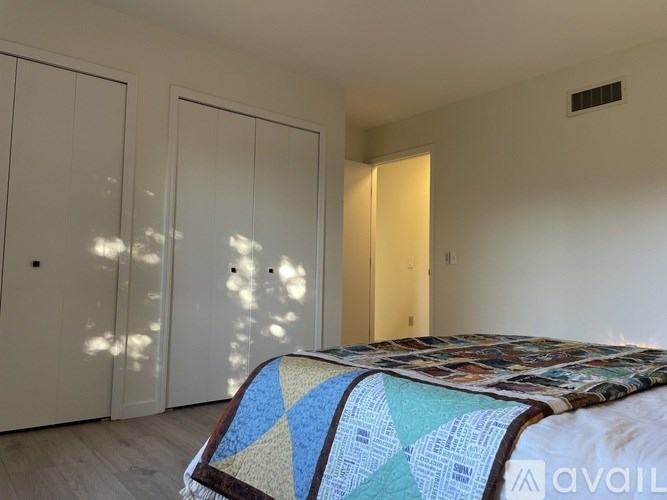 A bed with a quilt on it is in a room with a white wall and a door.