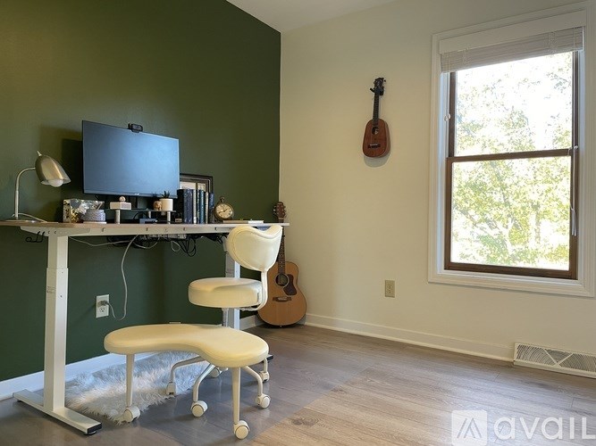 A room with a desk, chair, and a guitar hanging on the wall.