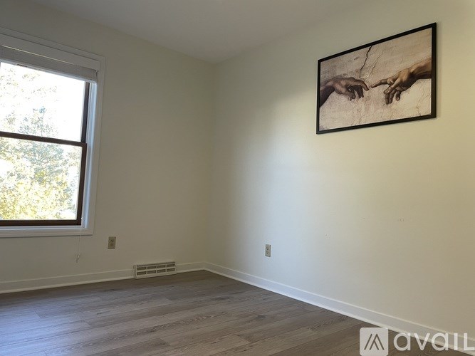 A room with a framed picture of two hands on the wall and a window letting in light.