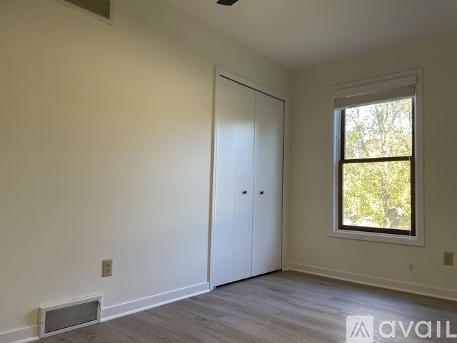 A room with a white door and a window with a view of trees outside.