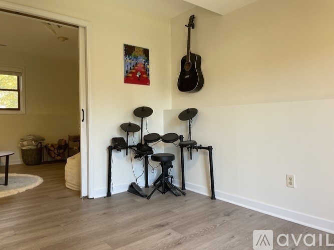 A room with a guitar hanging on the wall and a drum set on the floor.
