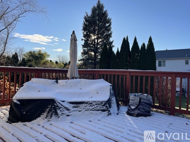 A snow-covered deck with a black umbrella and a black bag.