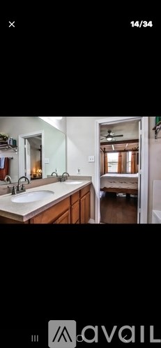 A bathroom with a sink, mirror, and a bed in the background.