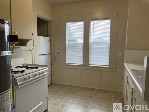 A kitchen with a stove, refrigerator, and a window with blinds.