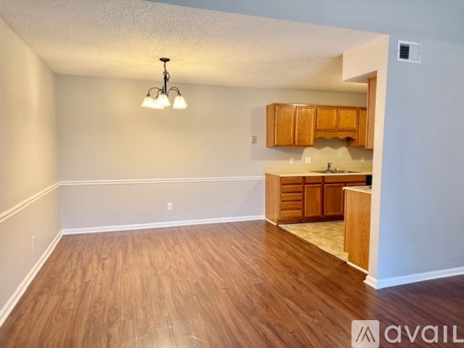 A room with wooden floors and a kitchenette in the background.