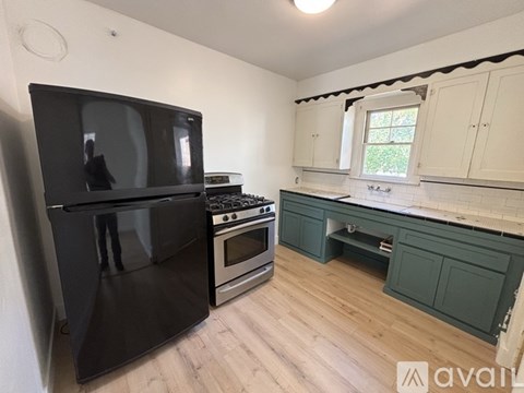 A black fridge stands in a kitchen with wooden floors and white walls.