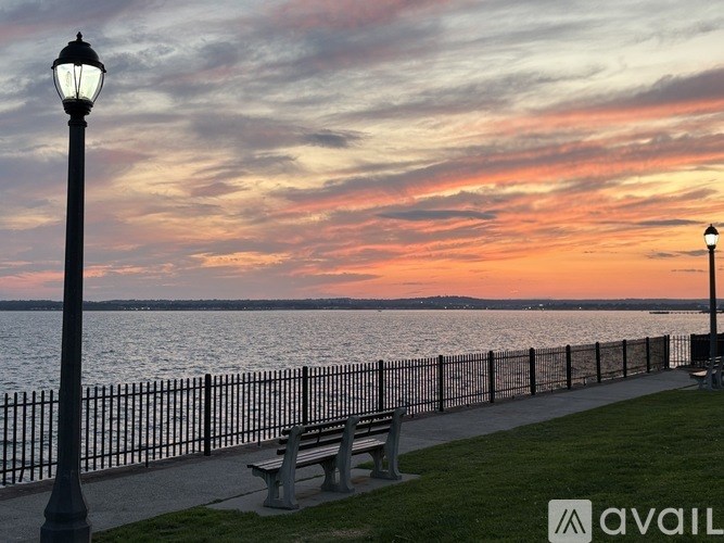 A park bench sits next to a lamp post on a path by the water.