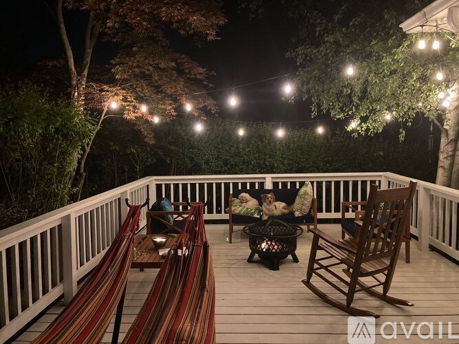 A deck with hammocks and chairs is lit by string lights.