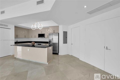 A modern kitchen with a central island and a refrigerator to the left.