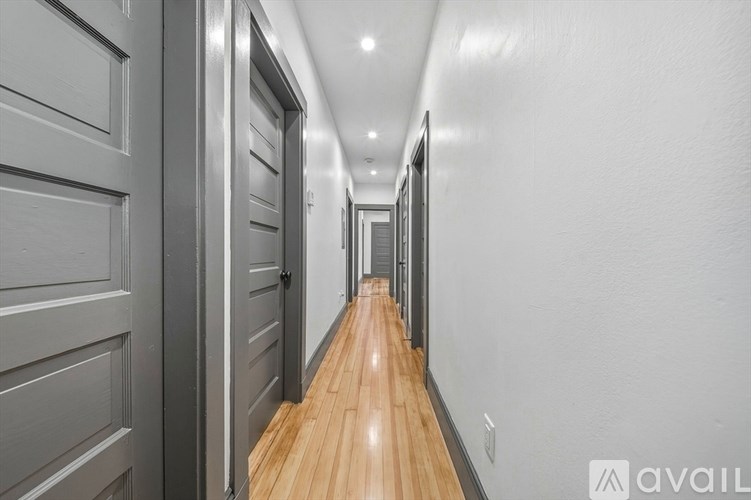 A long hallway with doors on the left and a wooden floor.