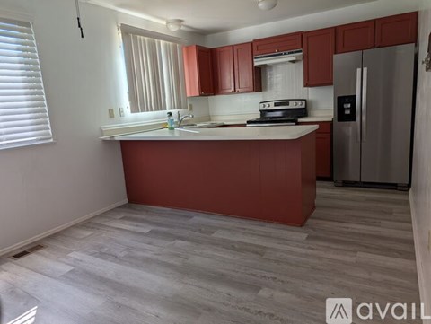 A kitchen with red cabinets and a stainless steel refrigerator.