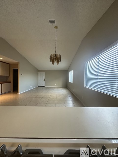 A chandelier hangs from the ceiling in a room with a window covered in blinds.