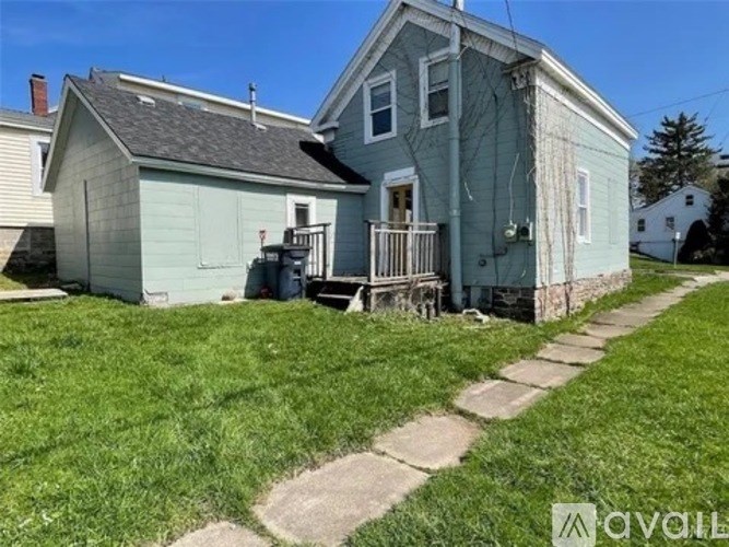 A small house with a porch and a trash can on the lawn.