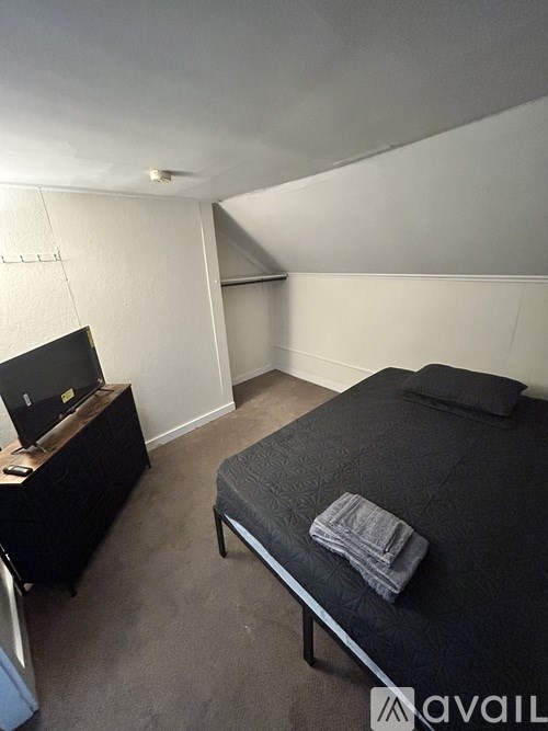 A bedroom with a bed, a desk with a laptop, and a wall-mounted shelf.