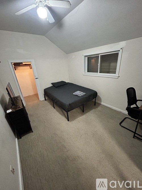 A bedroom with a bed, chair, and ceiling fan.