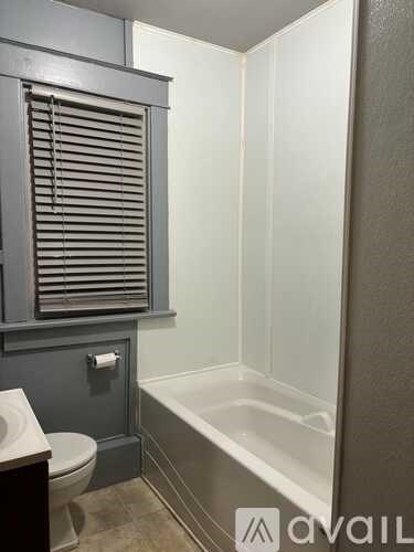A bathroom with a toilet, a bathtub, and a window with blinds.