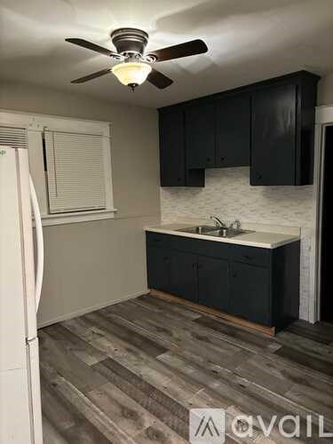 A kitchen with a white fridge, black cabinets, and a ceiling fan.