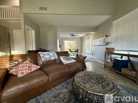 A living room with a brown leather couch and a round woven ottoman.