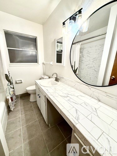 A white bathroom with a marble counter top and a round mirror.